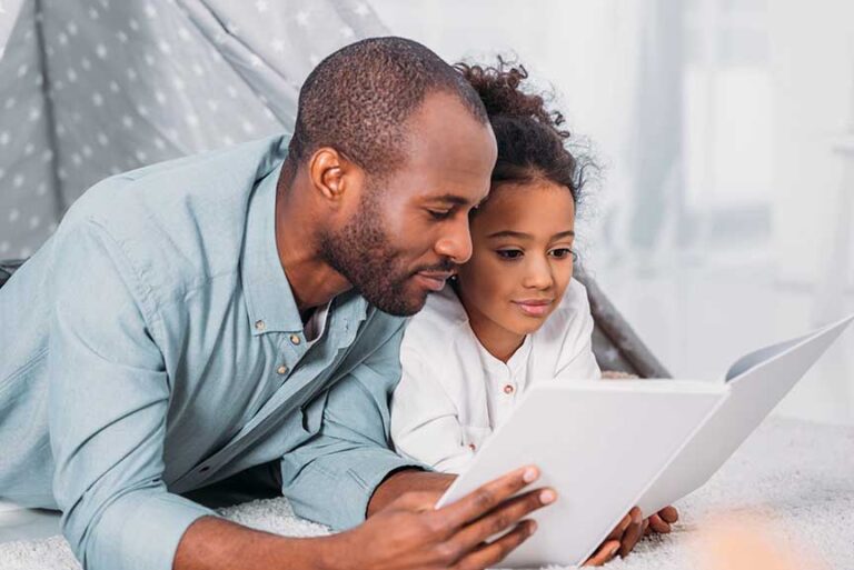 father and daughter lying on floor and reading together at home