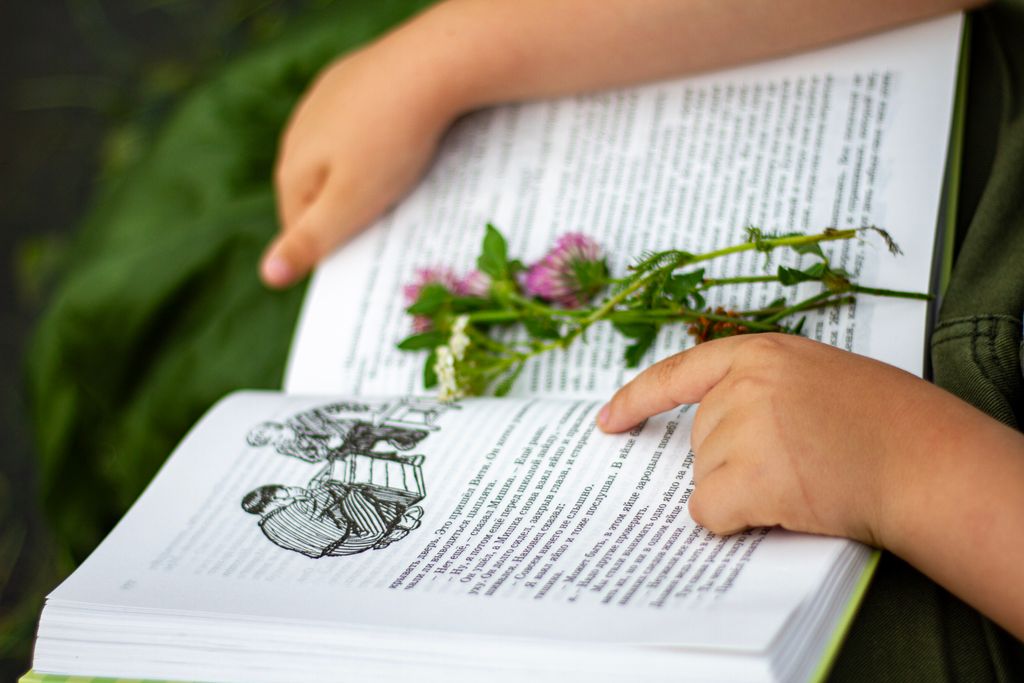A child reading an open book with wildflowers placed on the pages, outdoors.