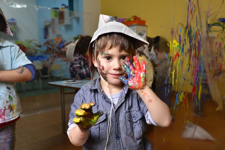 A joyful child with painted hands participates in a vibrant art class, expressing creativity and fun.