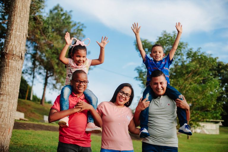 A joyful family spending quality time outdoors with kids on parents' shoulders.