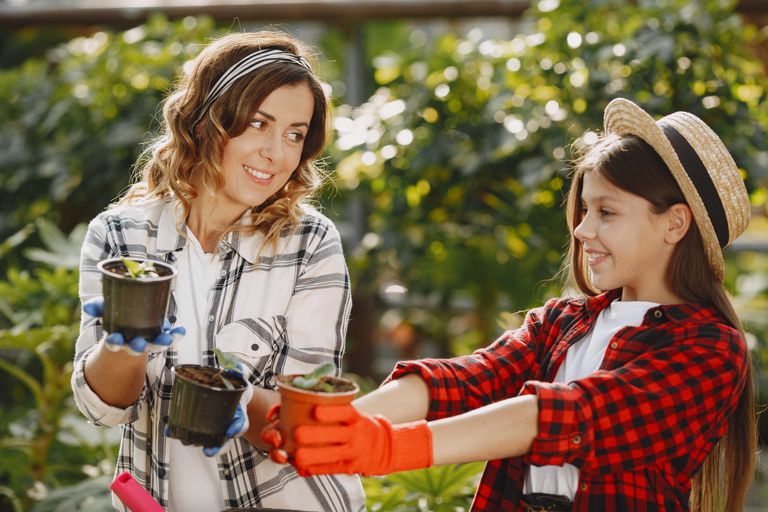A mother and daughter duo joyfully gardening outdoors, sharing potted plants.