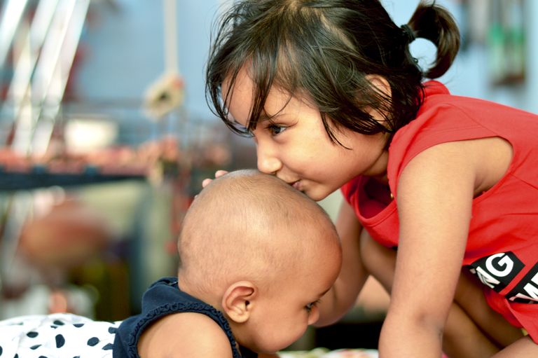 A touching moment of sisterhood as a young girl gently kisses her baby brother's head indoors.