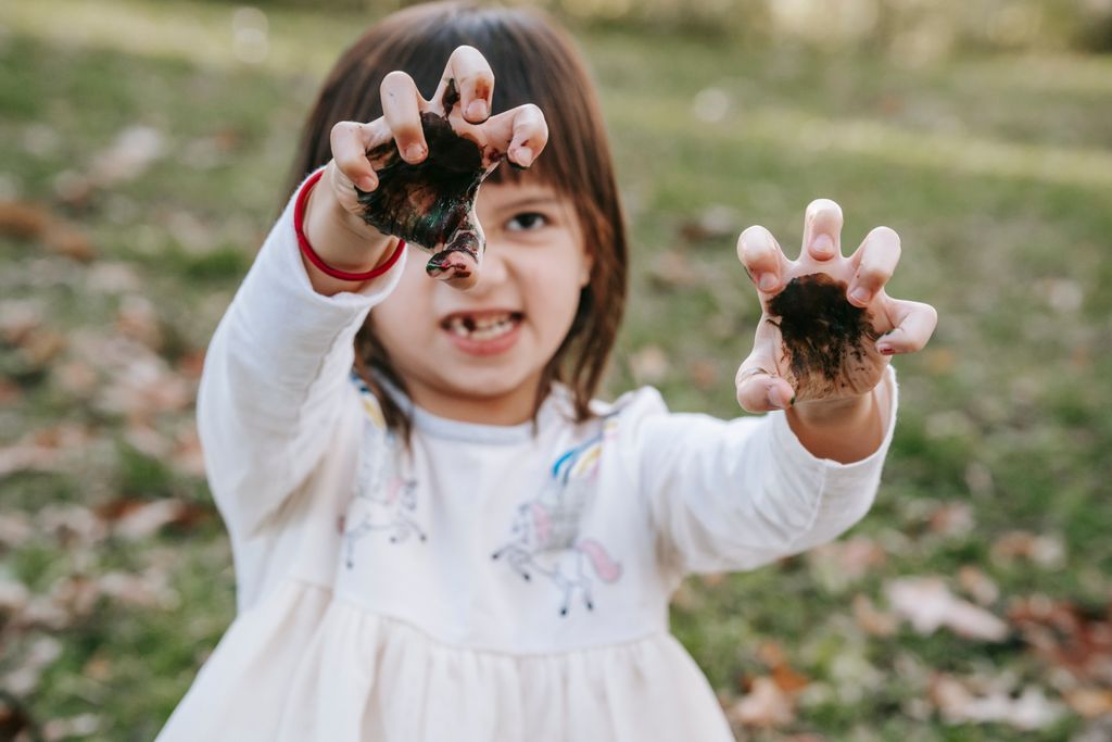 Funny girl with painted hands making scary face while playing in park during Halloween celebration