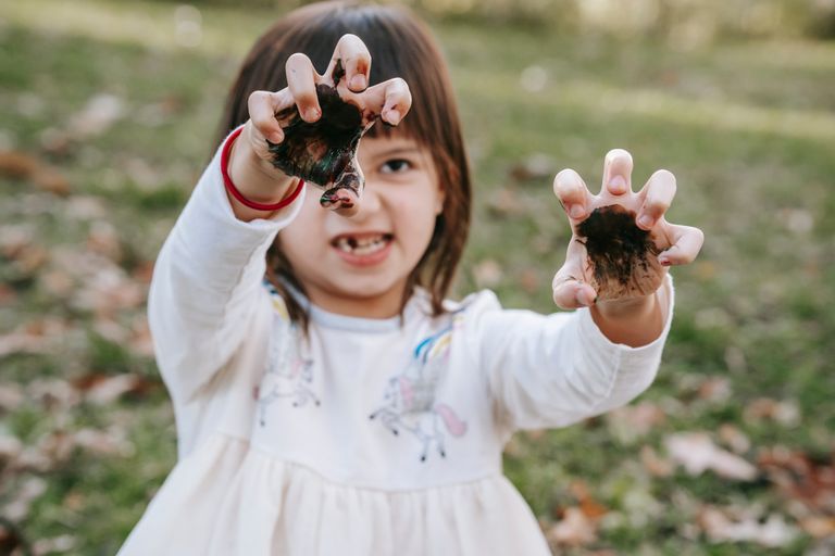 Funny girl with painted hands making scary face while playing in park during Halloween celebration