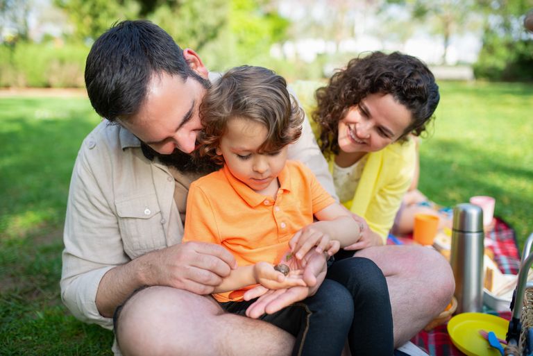 Happy family bonding at a sunny outdoor picnic with their son, enjoying quality time together.