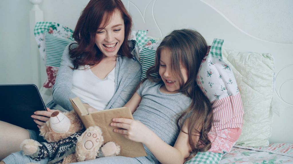 Mother and daughter enjoying a cozy reading time together in a bedroom.