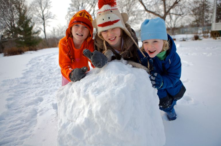 Three children joyfully building a snowman on a snowy day in Ontario, Canada.