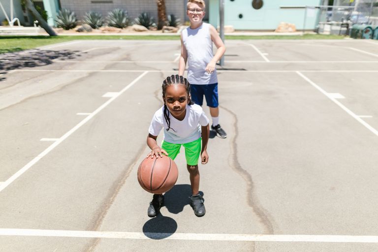Two children playing basketball on an outdoor court during the day.
