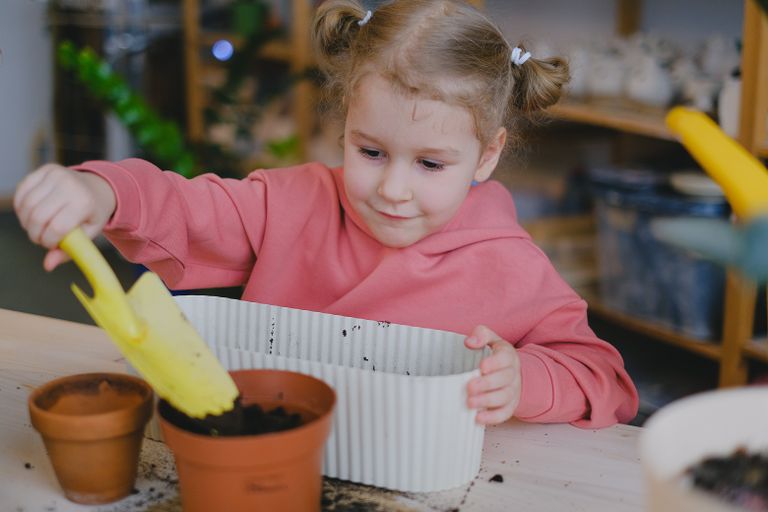 Young girl planting indoors with soil and pots, learning gardening.