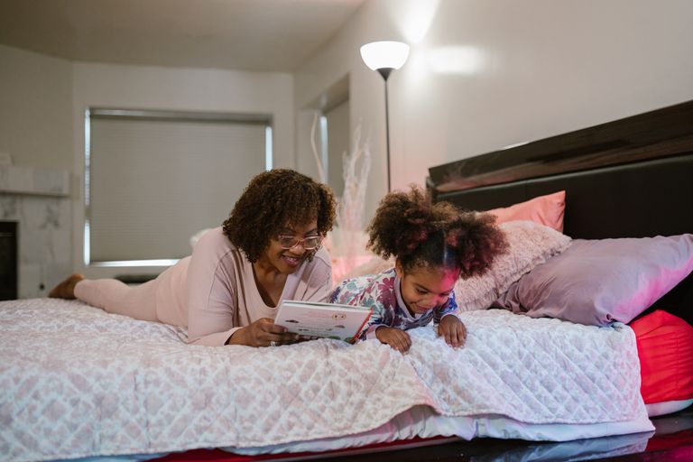 A joyful moment with a mother and daughter reading together on a bed in a cozy indoor setting.